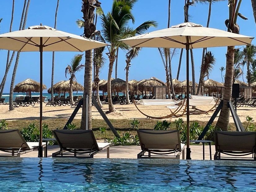 A swimming pool surrounded by chairs and umbrellas with a beach in the background