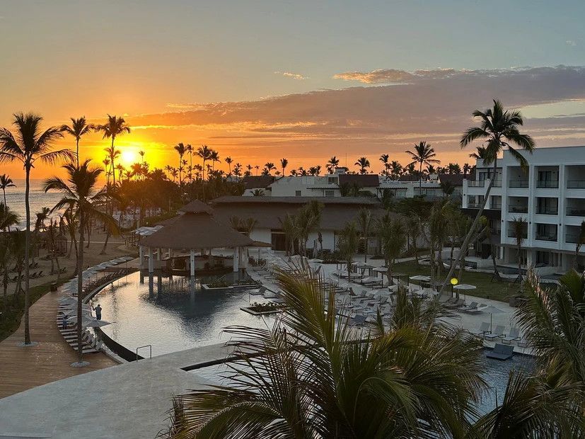 A sunset over a resort with palm trees and a large pool