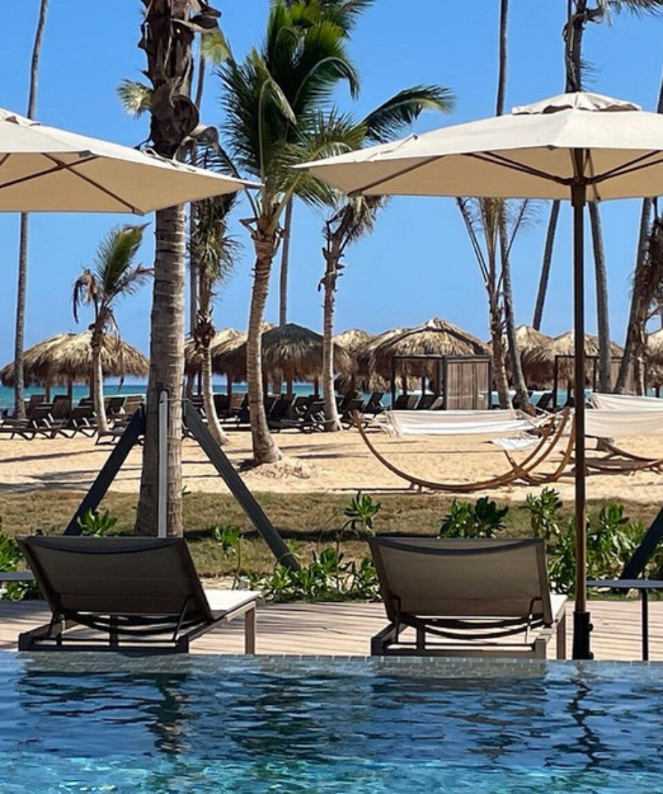 A swimming pool surrounded by chairs and umbrellas with a beach in the background