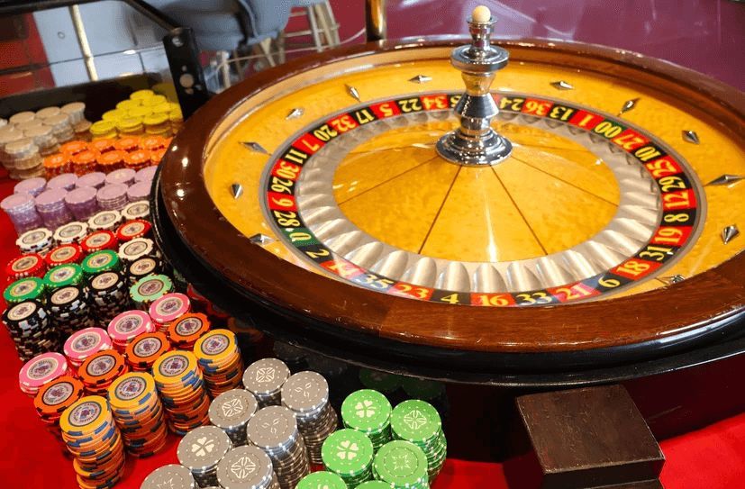 A roulette wheel is surrounded by poker chips on a red table.