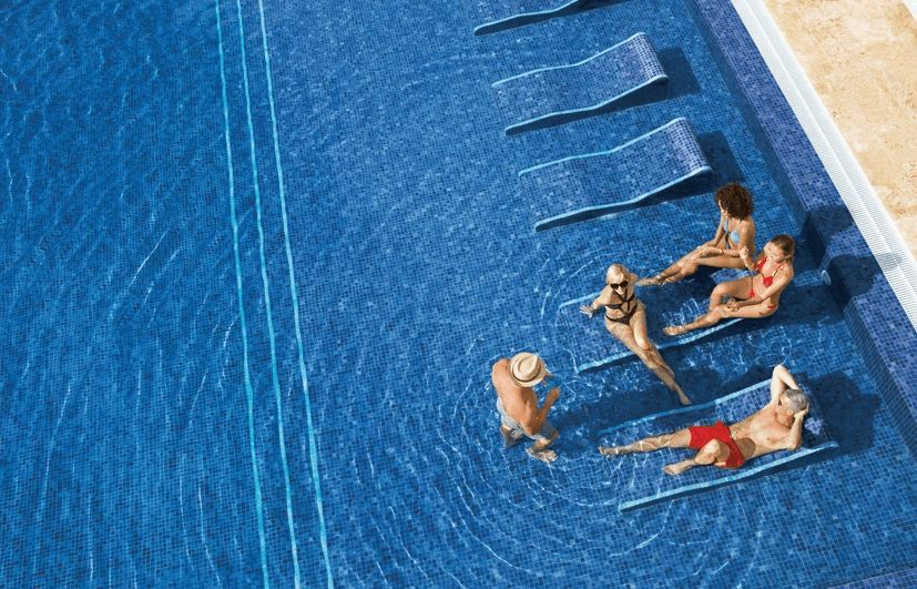 A group of people are sitting on lounge chairs in a swimming pool.
