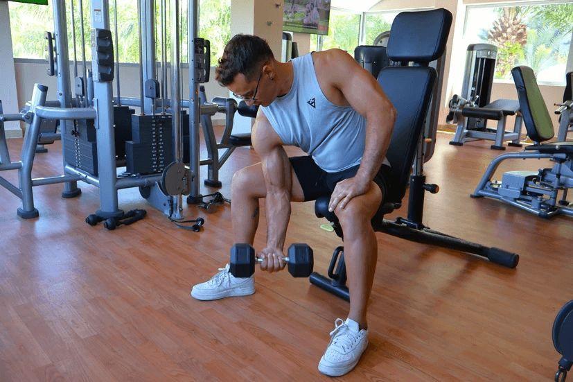 A man is sitting on a bench in a gym holding a dumbbell.
