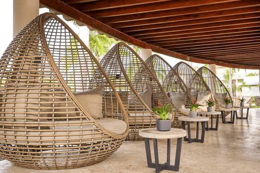 A row of wicker chairs and tables under a canopy.