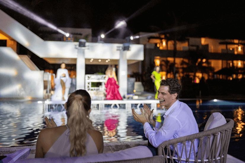 A man and a woman are sitting next to a swimming pool at night.