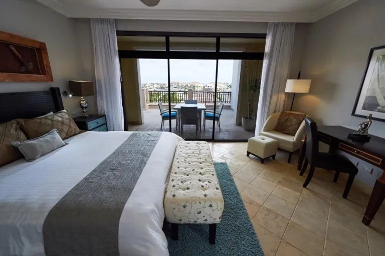 A hotel room with a large bed , chairs , desk and sliding glass doors leading to a balcony.