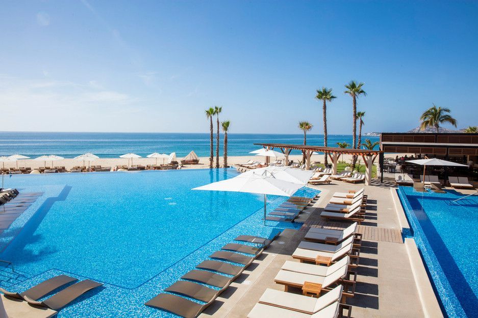 A large swimming pool surrounded by chairs and umbrellas next to the ocean.