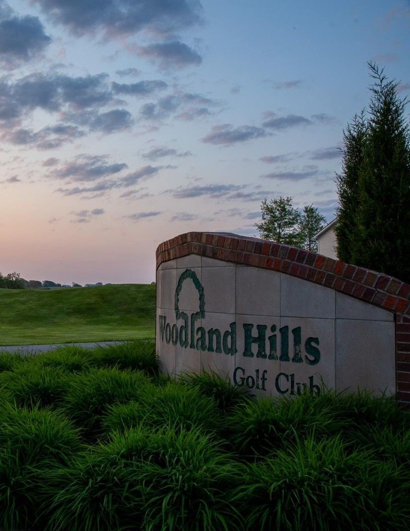 Aerial view of a scenic golf resort, Arabella Golf, with lush green fairways, sand bunkers, and surrounding trees under a hazy sky.