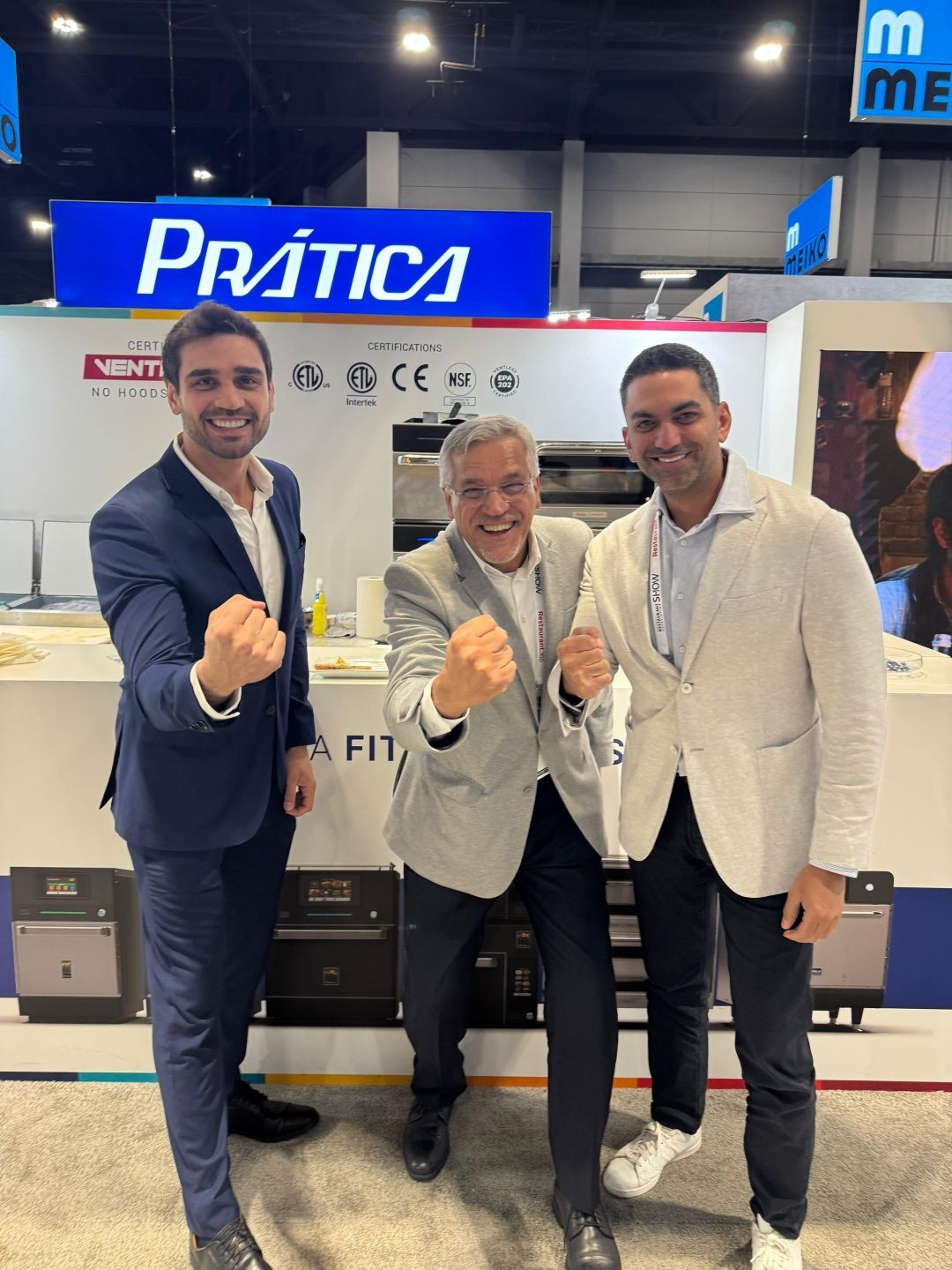 Three men at a trade show booth, fists raised in excitement, under the