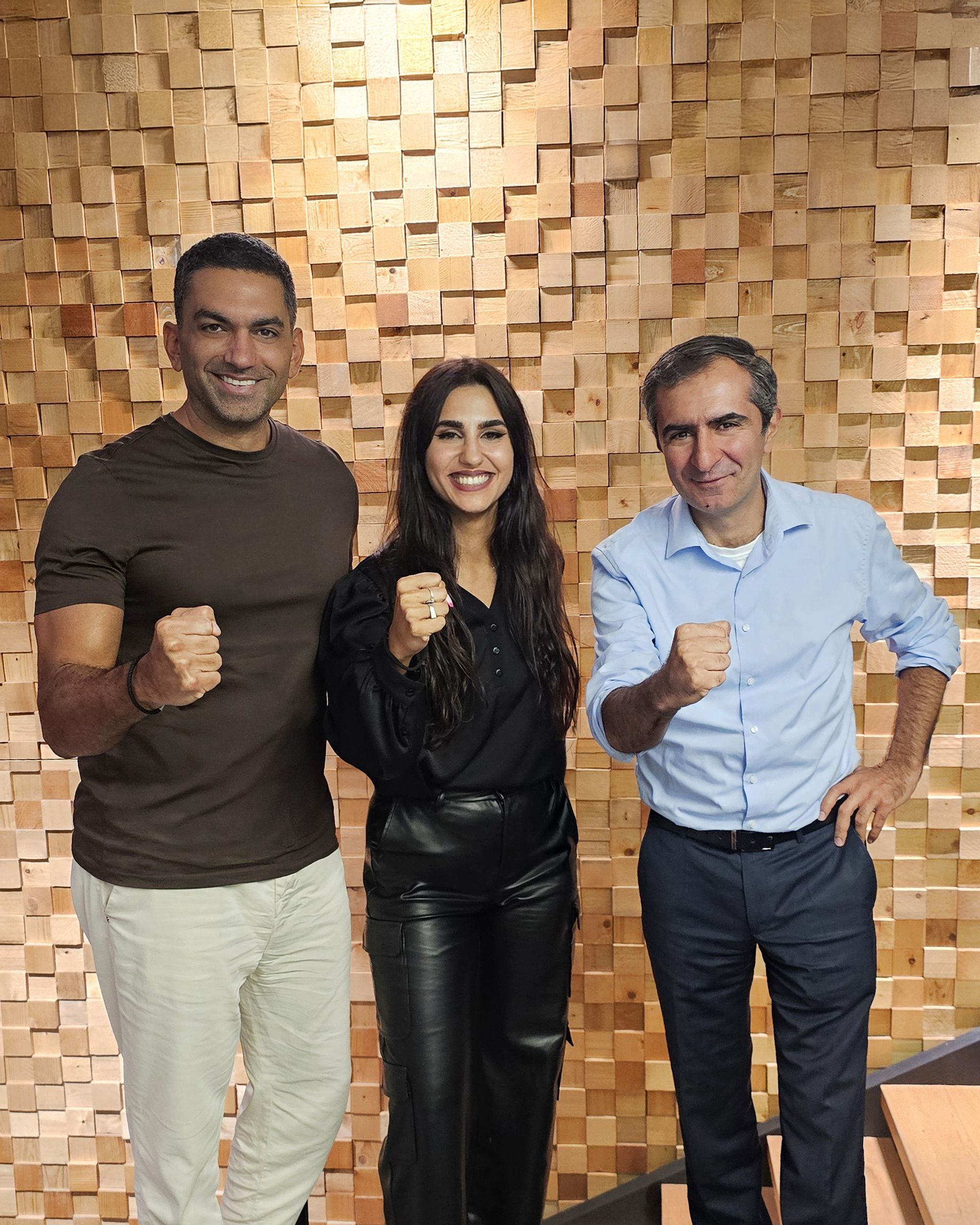 Three people posing, fists raised, in front of a wooden wall.