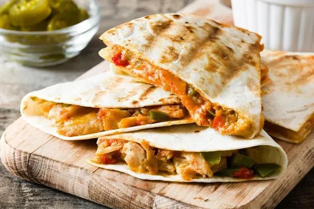 Three quesadillas are stacked on top of each other on a wooden cutting board.