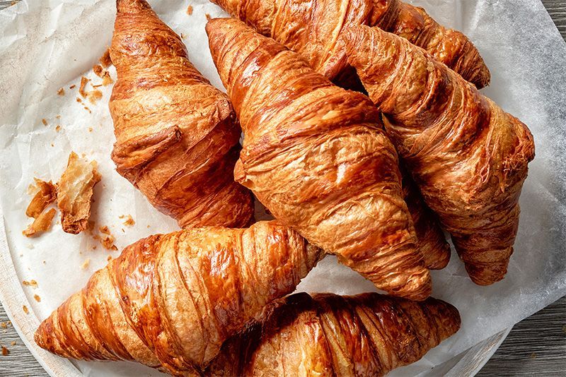 Three croissants are sitting on a wooden cutting board.