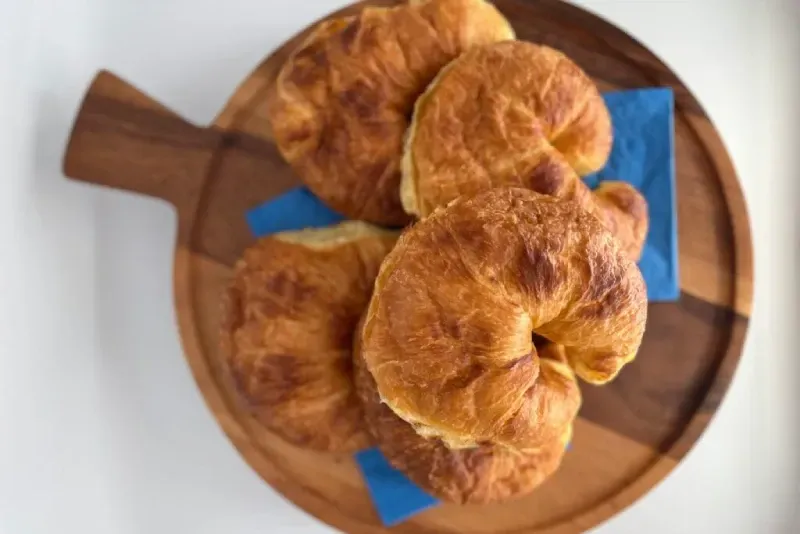 Three croissants are sitting on a wooden cutting board.