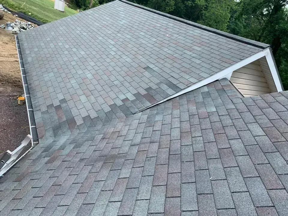 Gray and brown shingle roof, partially damaged, on a house with a white trim.