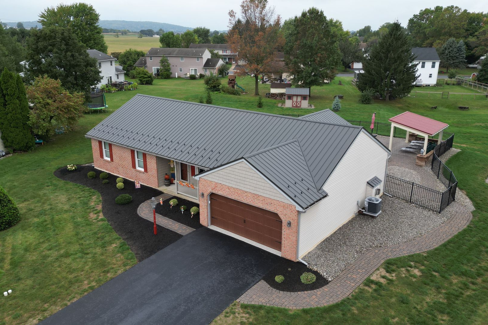 Aerial view of a ranch-style house with a gray roof and brown garage door; lush green lawn.