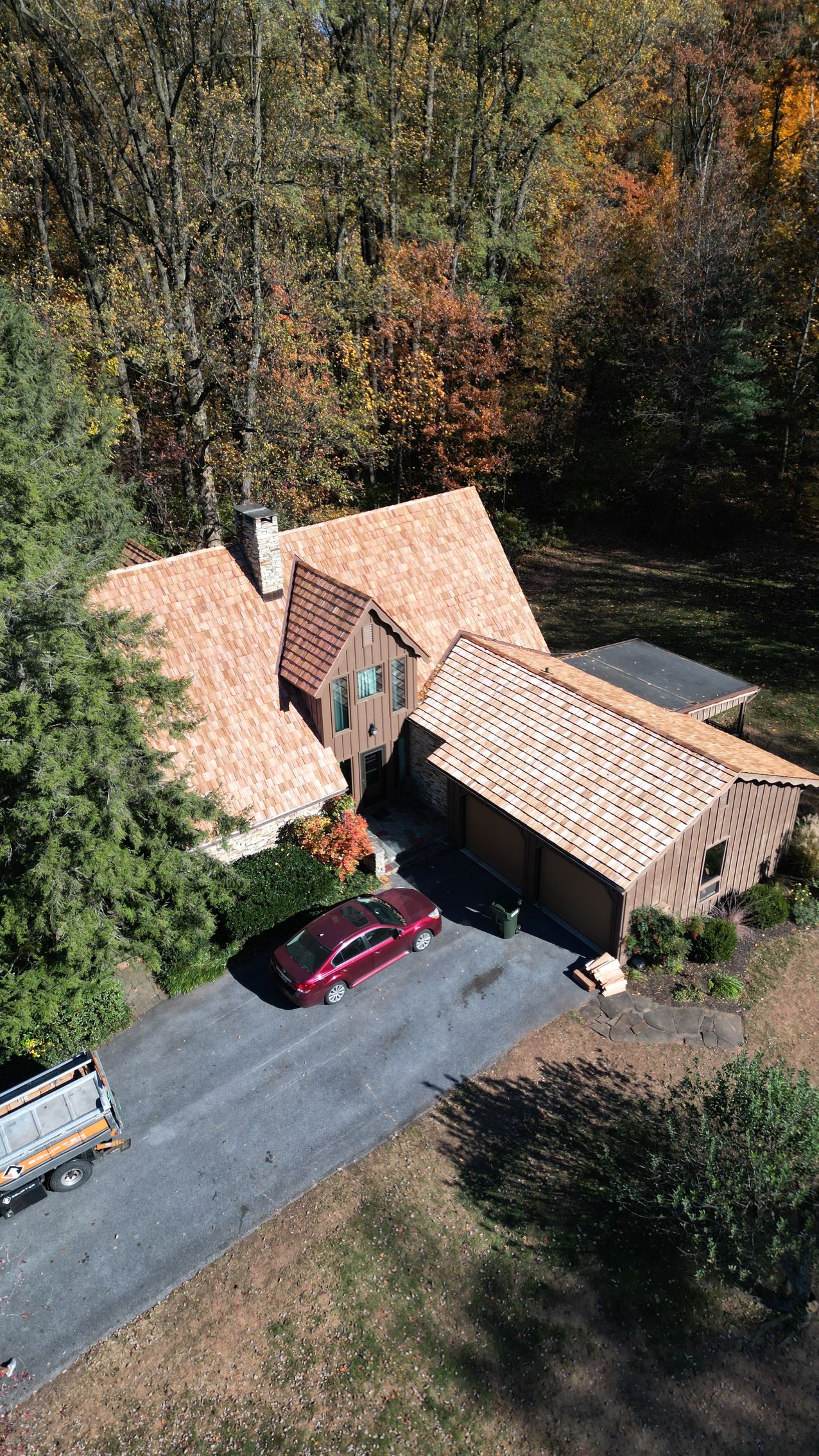 House with red car in driveway, surrounded by autumn trees. New roof installed.