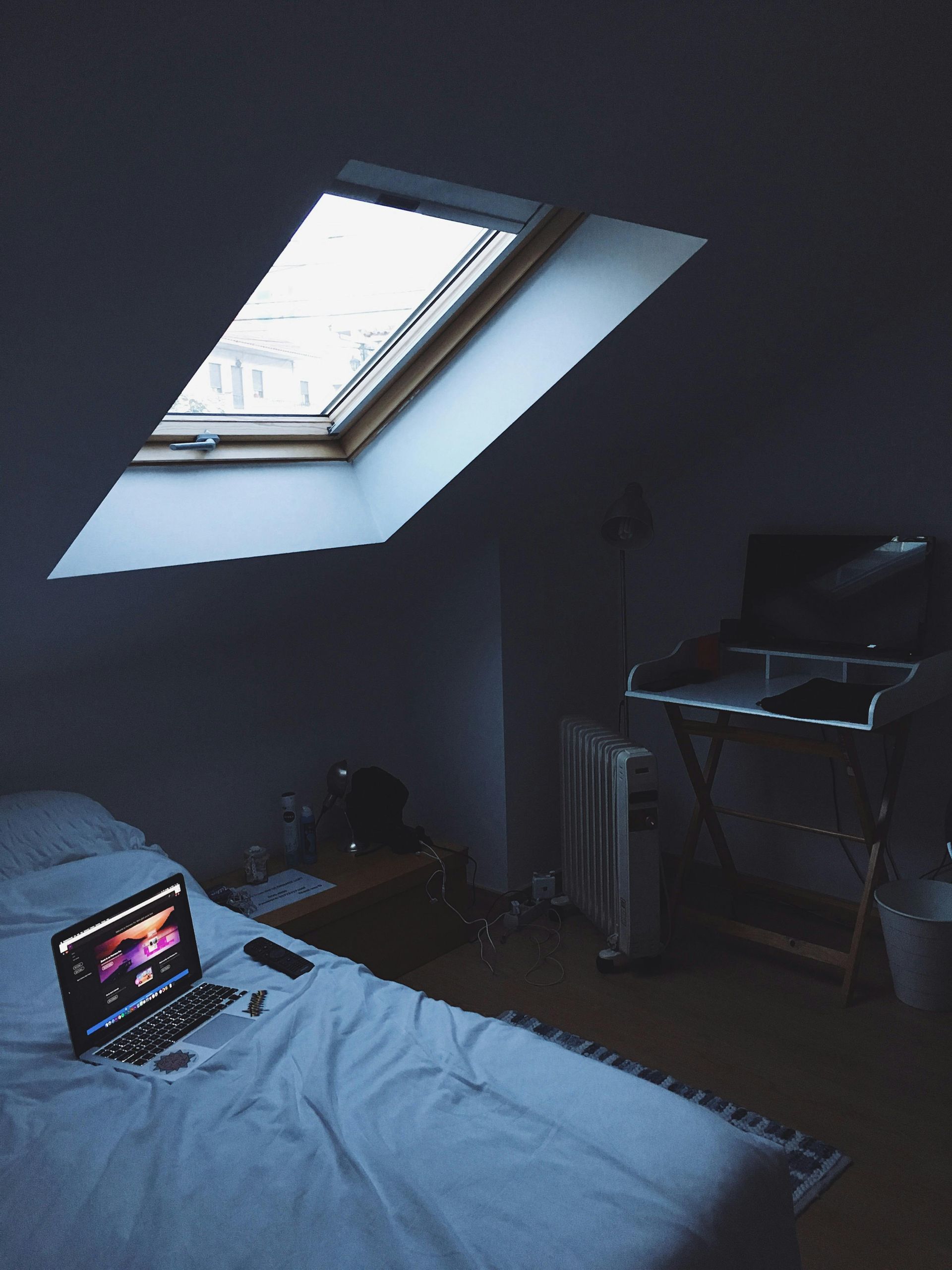 Cozy attic room with a laptop on a bed, lit by a skylight.