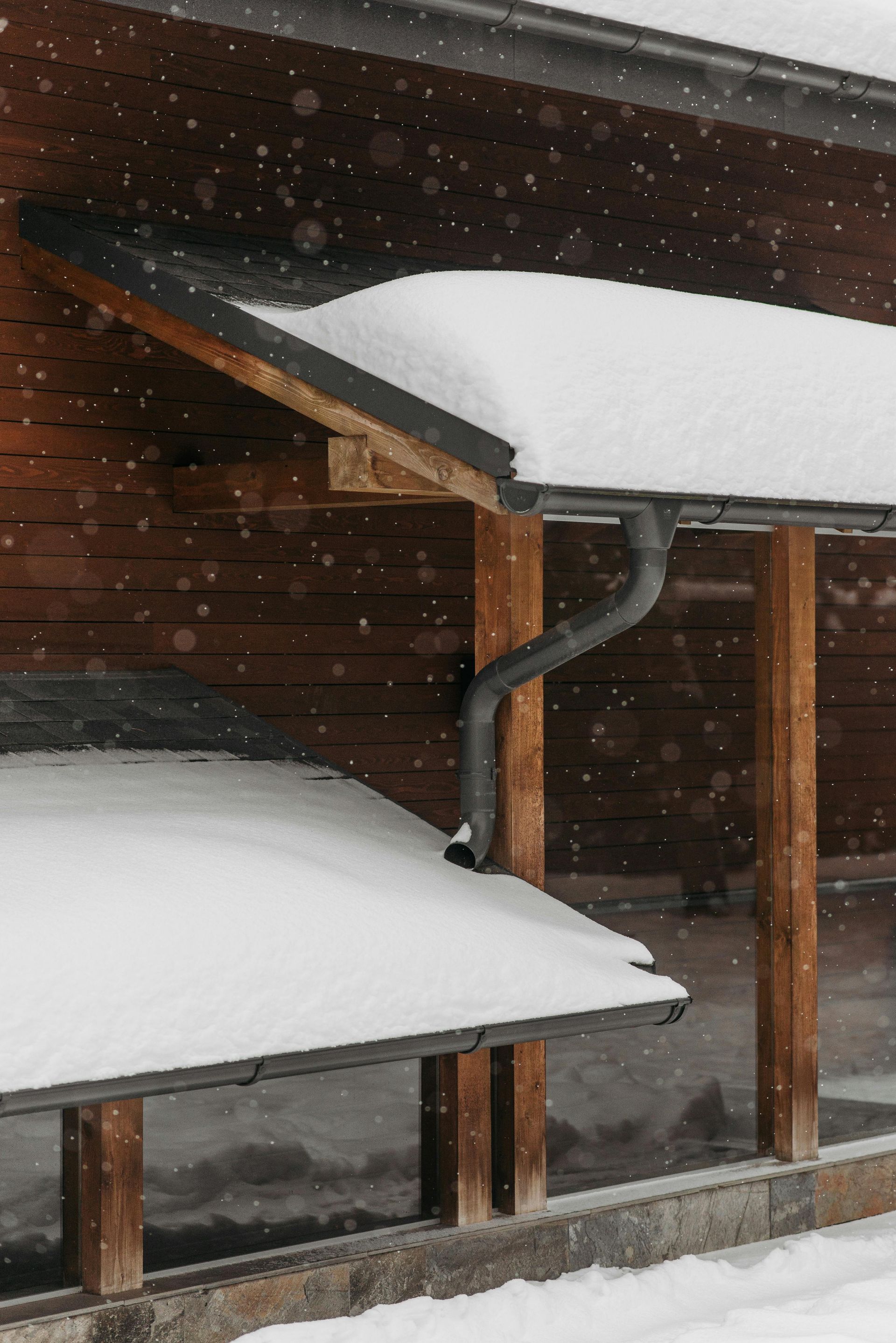 Snow-covered roof and gutter on a wooden building during a snowfall.