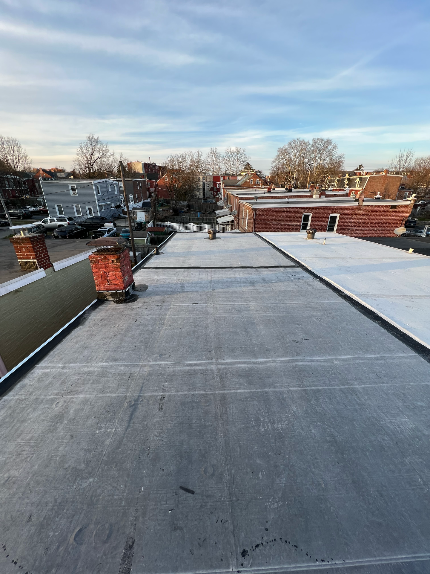 Rooftop view: gray flat roof, brick chimneys, distant buildings under a cloudy sky.