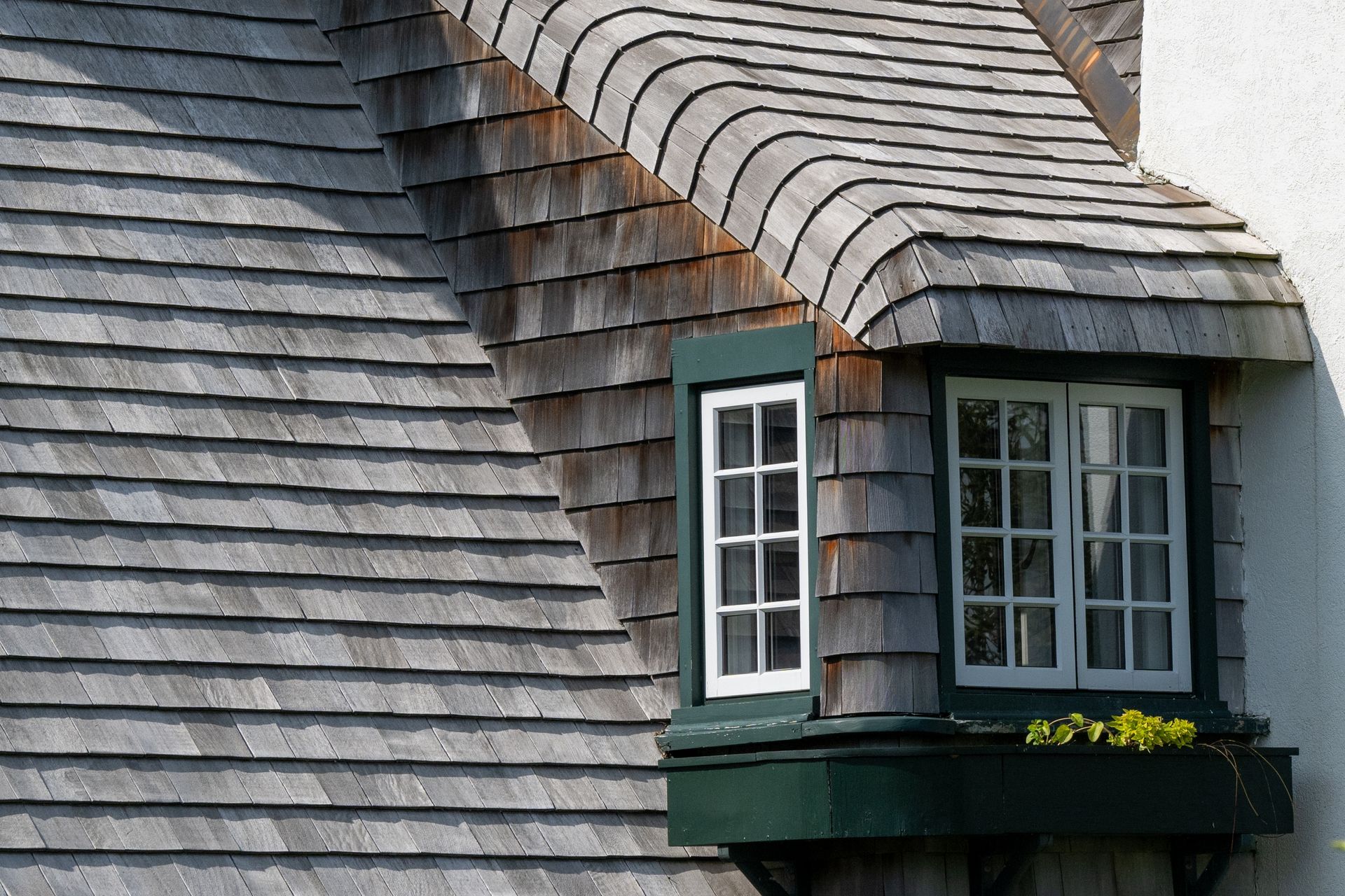 Wood-shingled roof with two windows and a small planter box, set against a white wall.