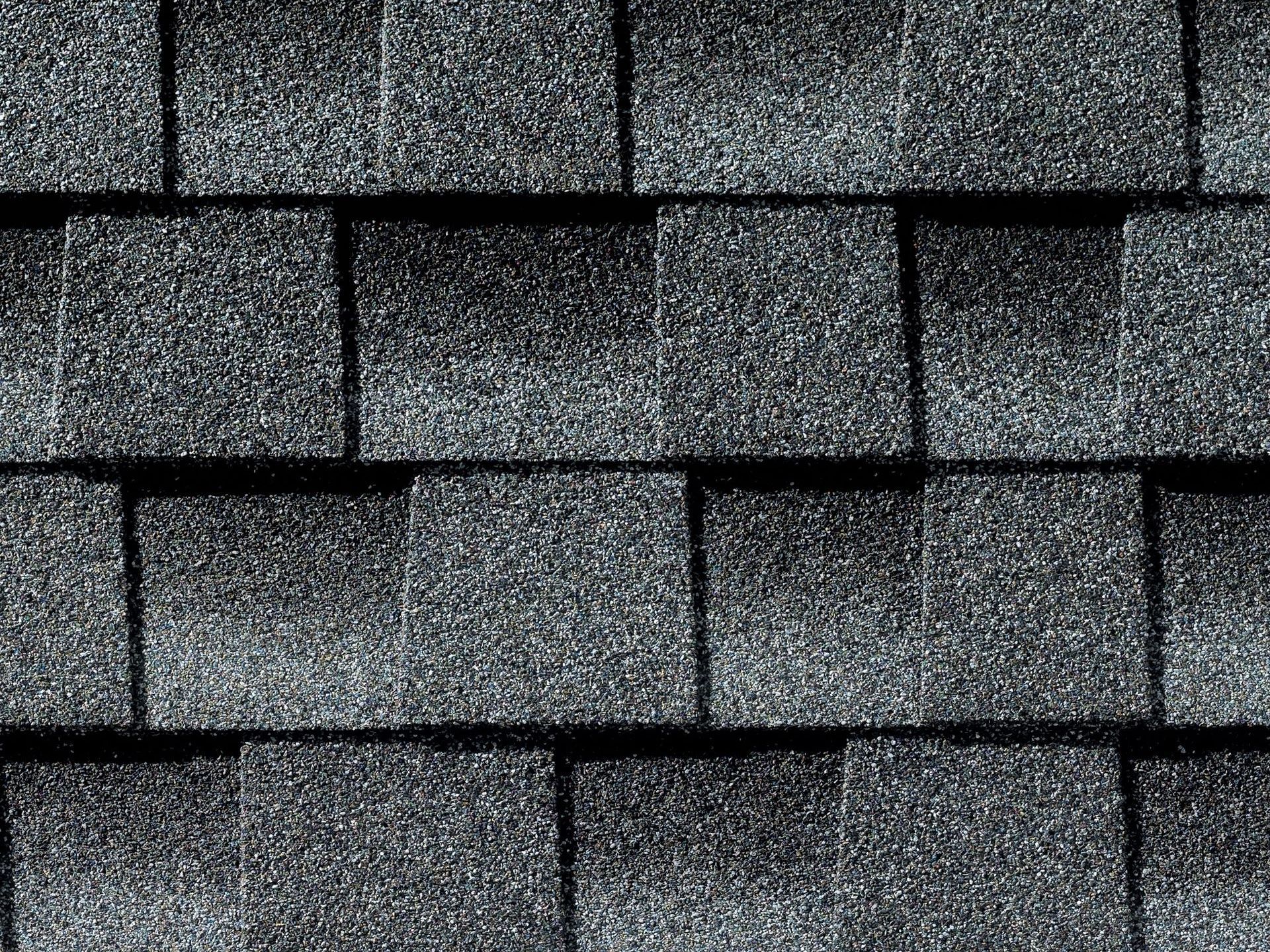 Close-up of overlapping gray asphalt roof shingles with a textured, granular surface.