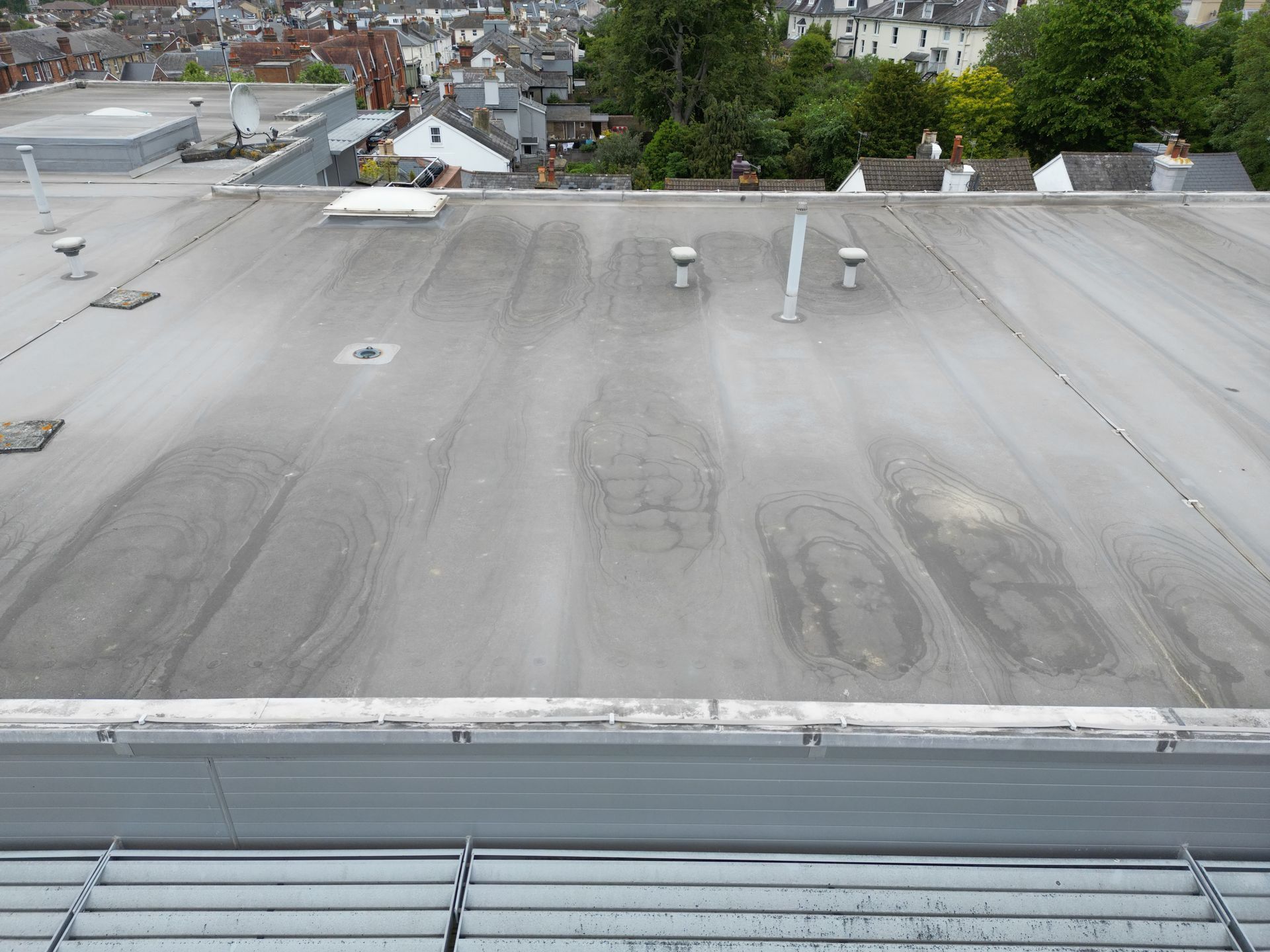Flat commercial roof with visible wear, vents, and a cityscape background.