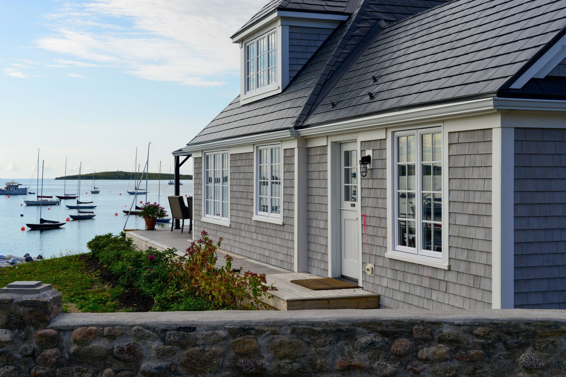 Gray shingled house with white trim, overlooking a harbor with boats.