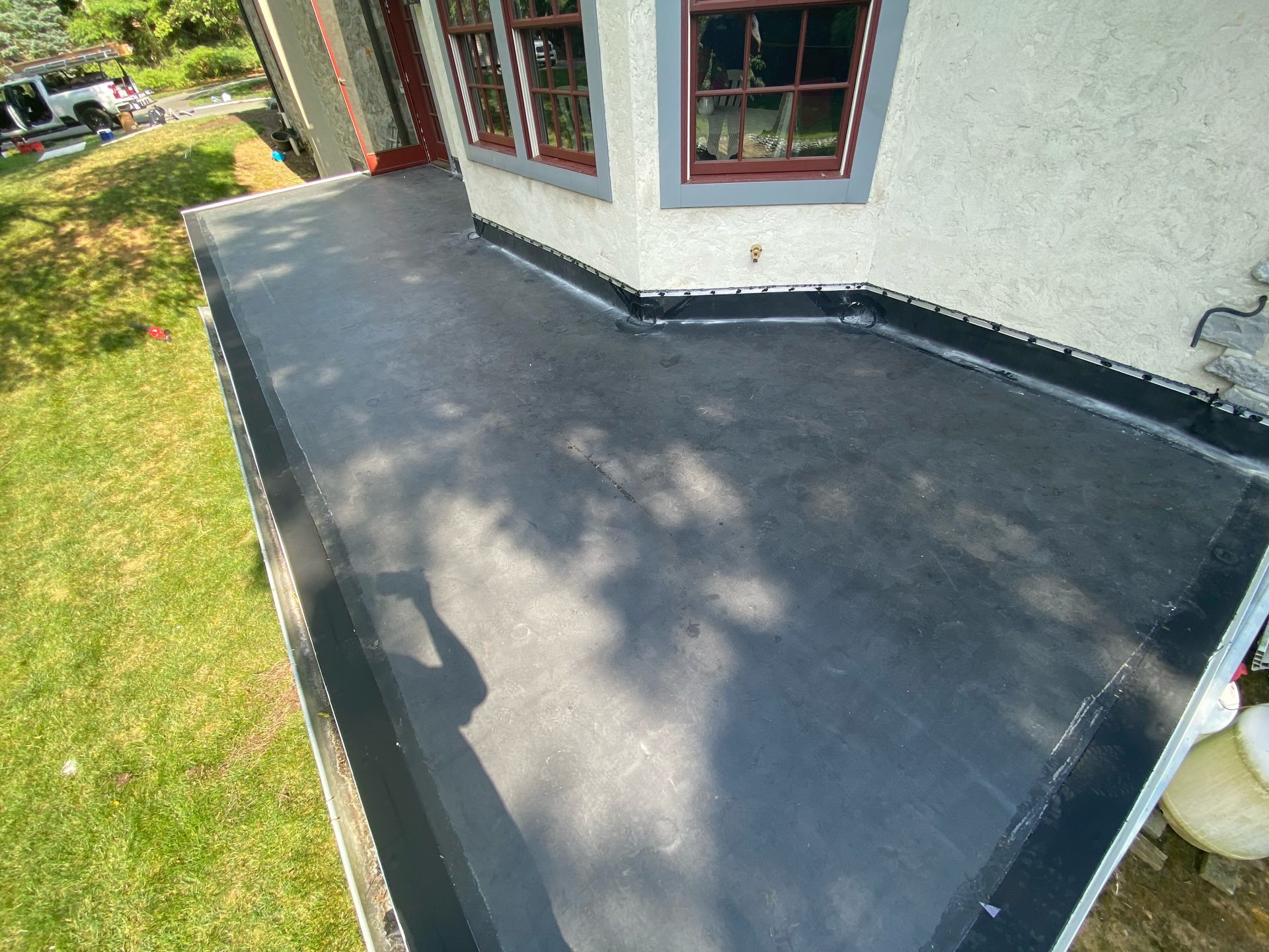 Black flat roof against a light-colored building with brown window frames, next to green lawn.