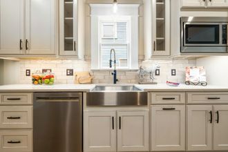 Stainless steel kitchen sink and appliances in a bright white kitchen with overhead lighting.