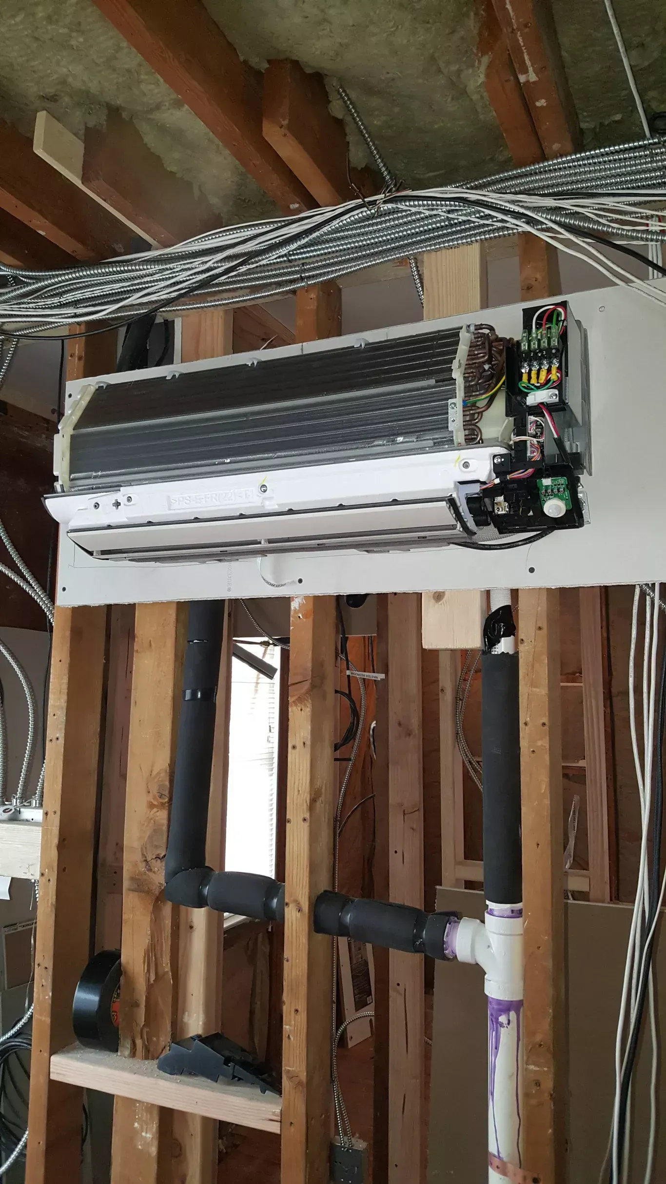 A wall mounted air conditioner is being installed in a house under construction.