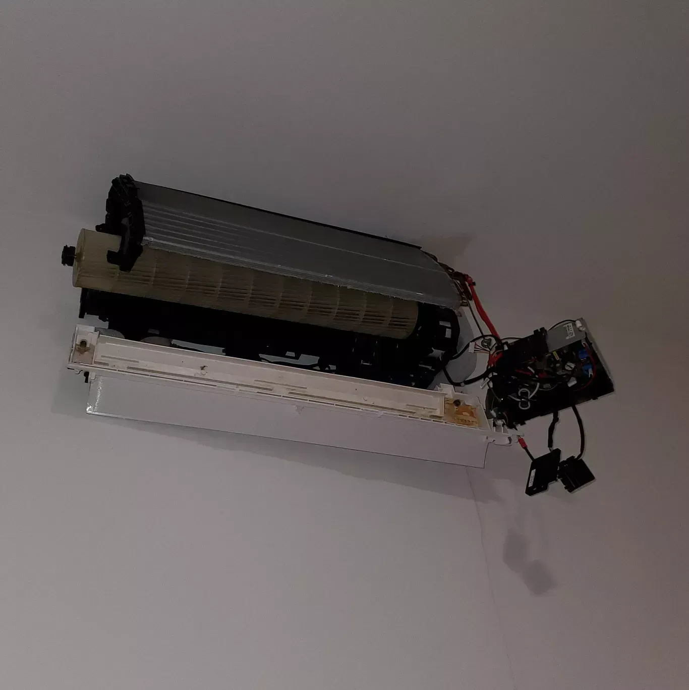 A broken air conditioner is hanging from the ceiling.