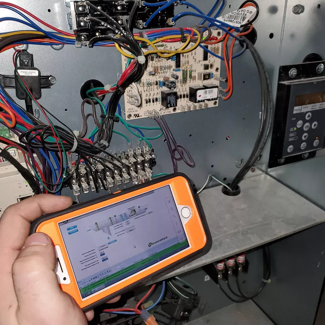 A person is holding a cell phone in front of a bunch of wires.