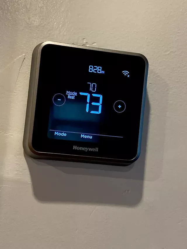 A smart thermostat is sitting on a white wall.