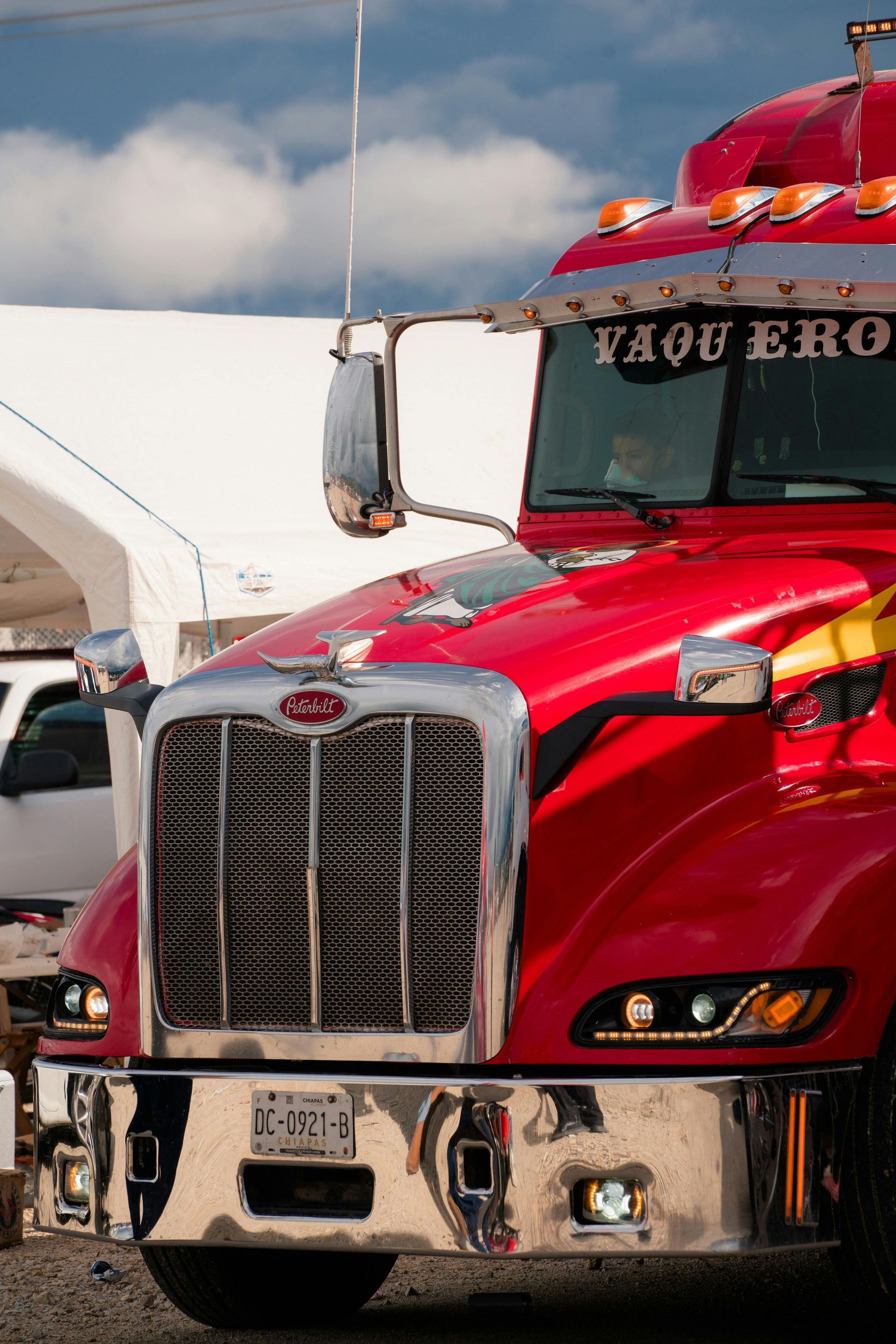 Three white semi-trucks parked on a highway, with a treeline in the background under sunlight.