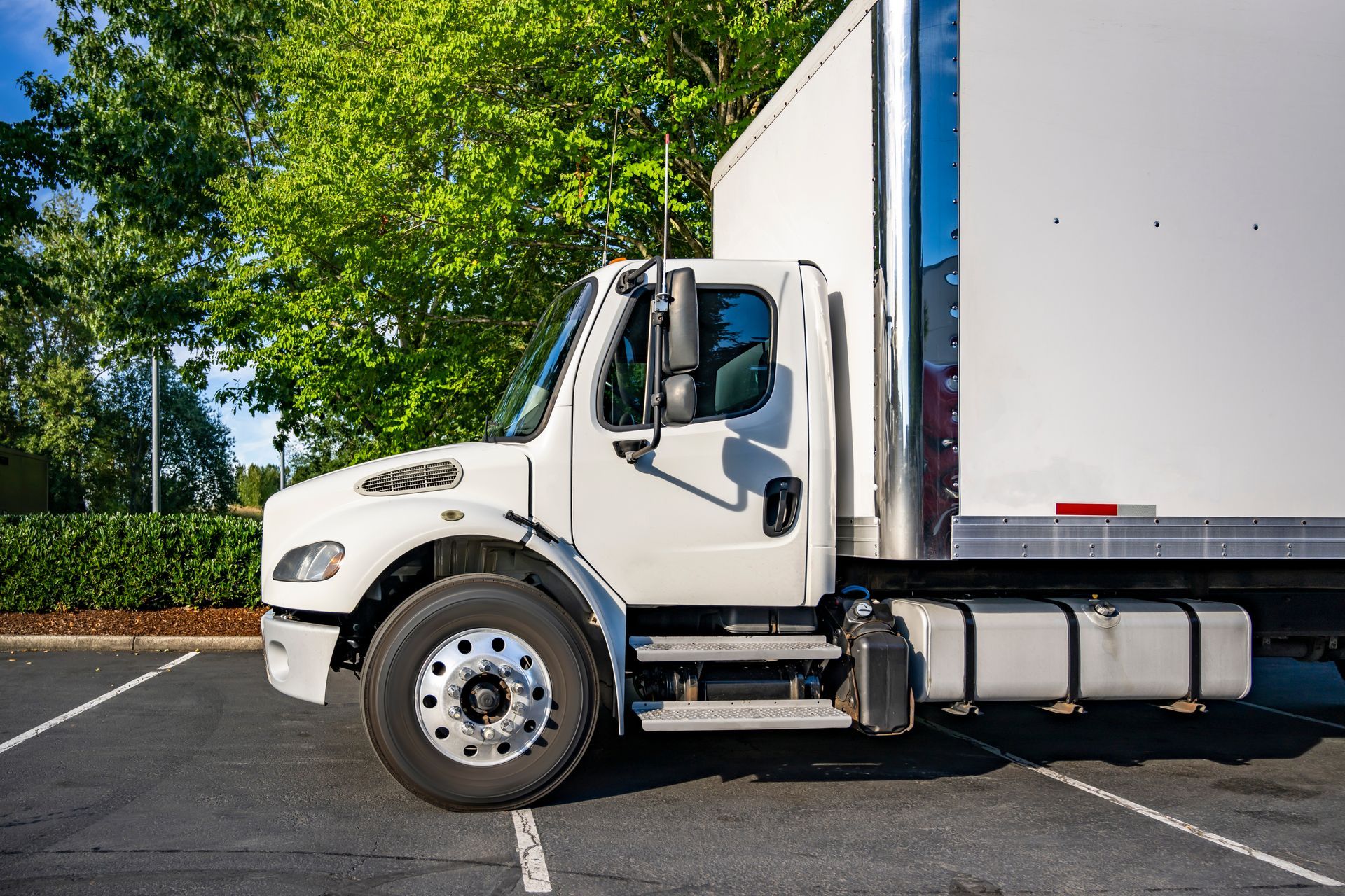 Three semi-trucks parked in a lot; light blue, gray, and white.