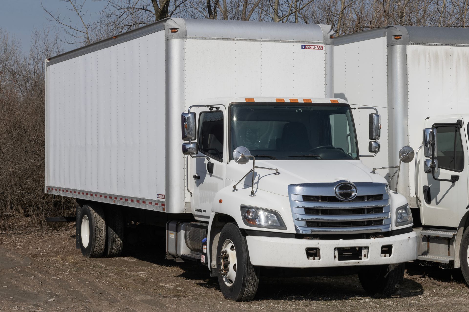 Black semi-truck on a two-lane road under a blue sky, driving on the right lane with a white trailer.