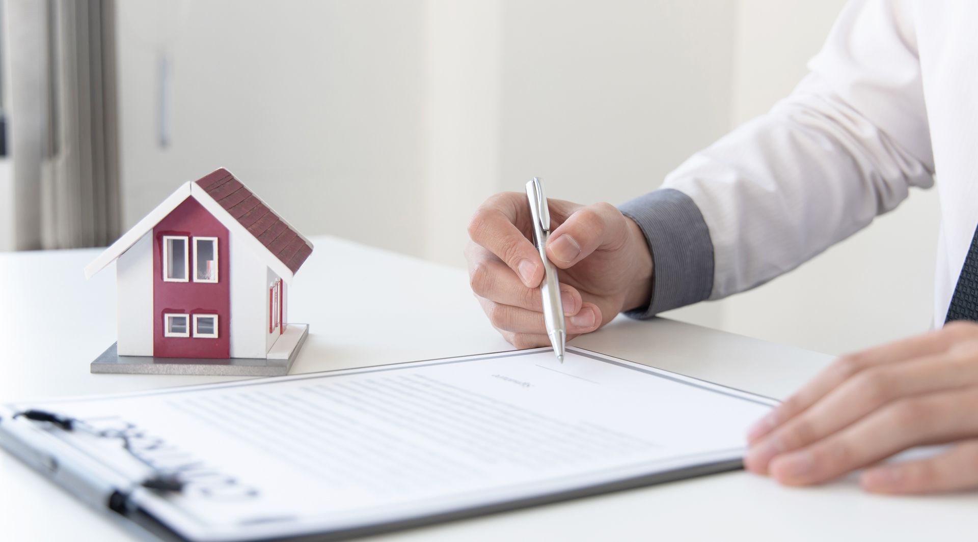 Person signing a document next to a model house
