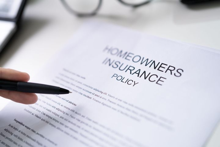Person holding pen pointing at a homeowner's insurance policy on a white table.
