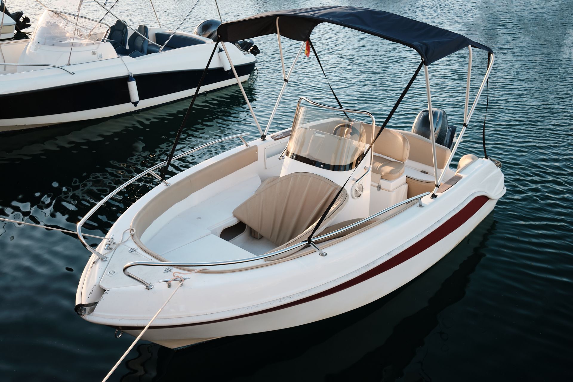 White motorboat with a dark blue canopy and red stripe, docked on calm water.