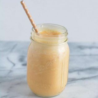 Orange smoothie in a mason jar with a straw on a marble surface.