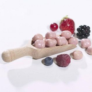 Pink chocolate candies in wooden scoop with fresh berries.