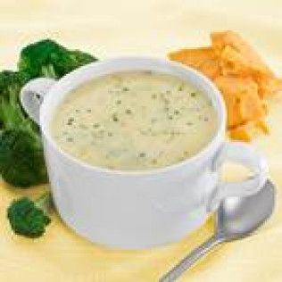 Broccoli cheddar soup in white mug, with broccoli florets, cheese crumbles, and spoon.