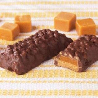 Chocolate-covered caramel candy bar with a caramel filling, on a yellow striped background with caramel cubes.