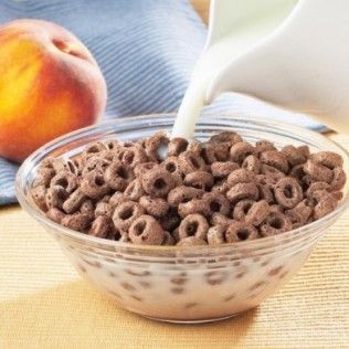 Milk being poured into a bowl of chocolate cereal, next to a peach.