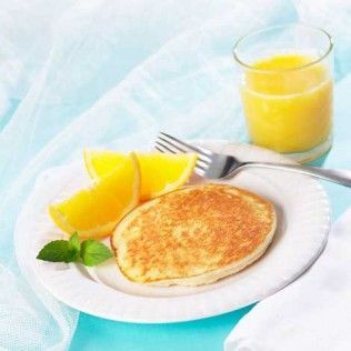 Pancake on a plate with orange slices, mint sprig, and a glass of orange juice.
