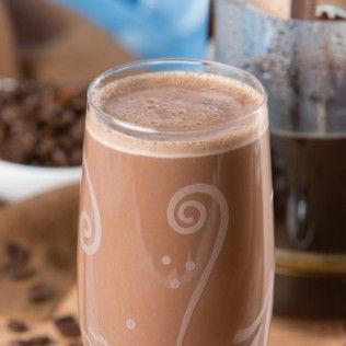 Tall glass of chocolate coffee drink with foamy top and etched design.