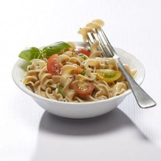 Pasta salad with cherry tomatoes and basil in a white bowl, fork with pasta.