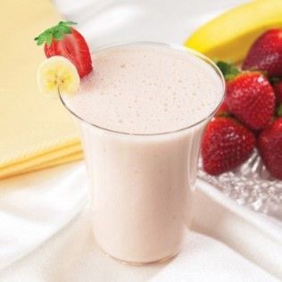 Strawberry banana smoothie in a glass, garnished with strawberry and banana slices, with fresh fruit in background.