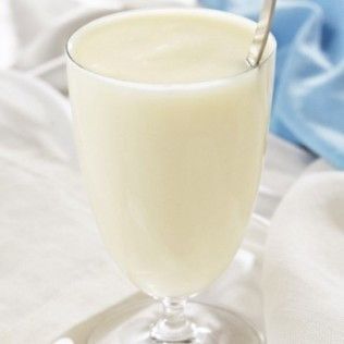 Glass of creamy, white drink with a spoon in it, set on a white tablecloth.