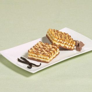 Two square pastries drizzled with chocolate on a white plate with vanilla beans and chocolate chunks.
