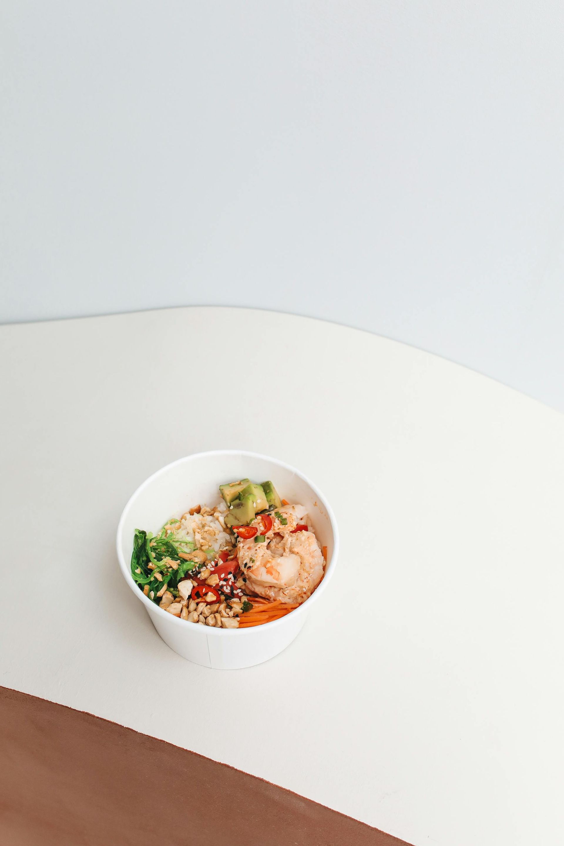 Bowl of colorful food on a white table; includes vegetables, rice, and what appears to be shrimp.